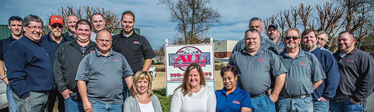 All Exterminating employee group photo in front of a sign promoting the company.